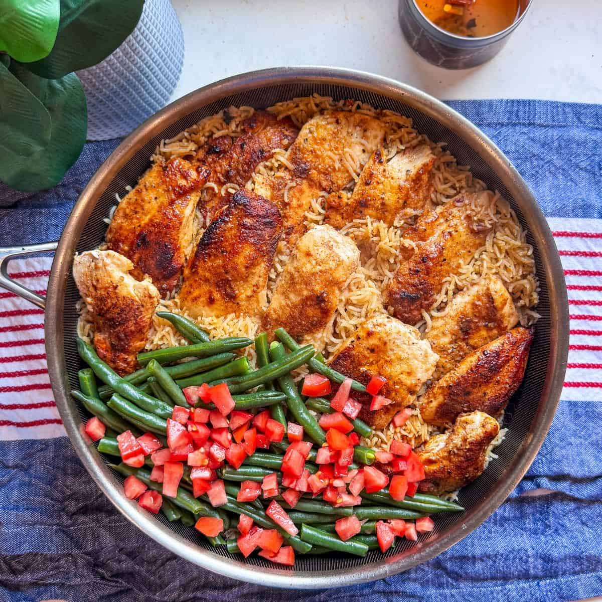 Chicken, rice, and green beans in a large skillet, freshly cooked and ready to serve.