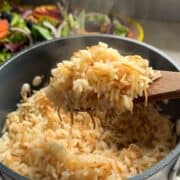 Overhead view of a wooden spoon scooping fluffy Armenian rice pilaf with toasted vermicelli from a pot