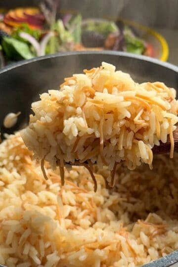 Overhead view of a wooden spoon scooping fluffy Armenian rice pilaf with toasted vermicelli from a pot