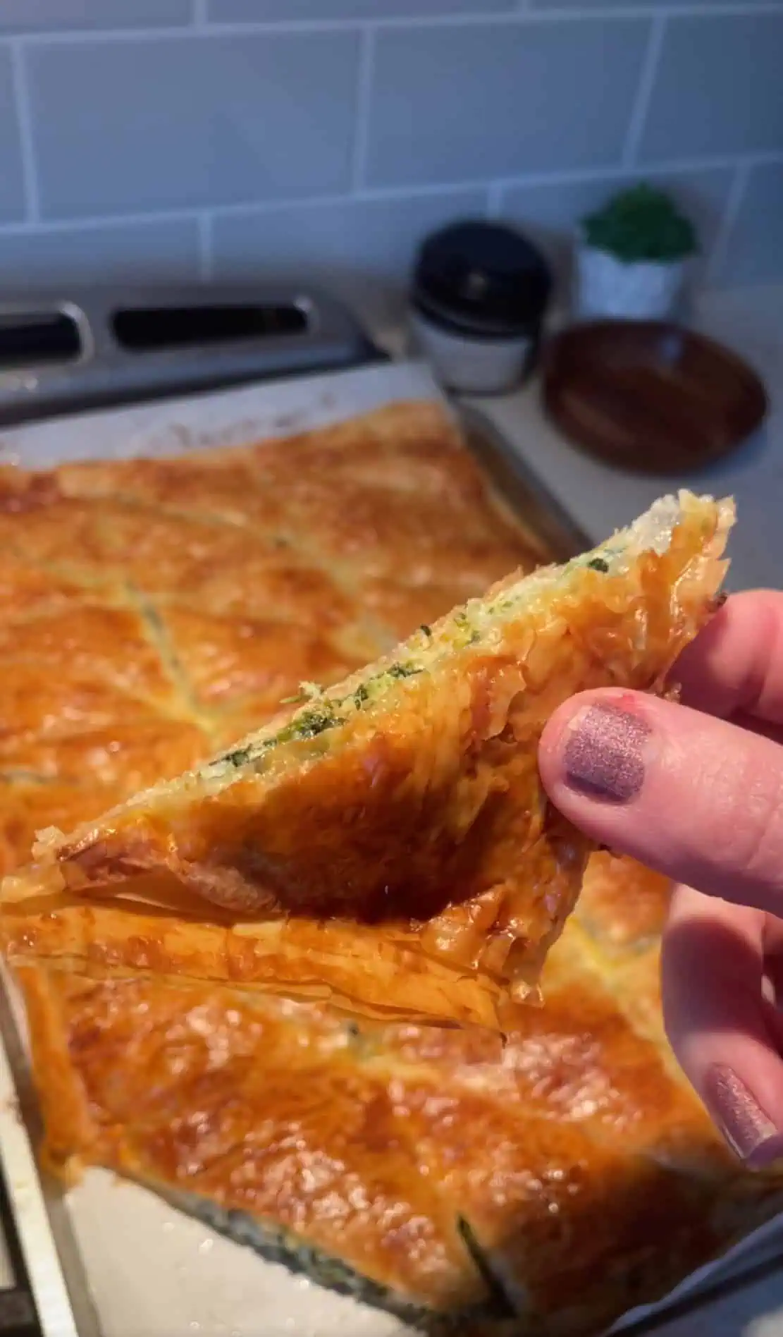 Hand holding a triangle slice of cheesy spinach pie