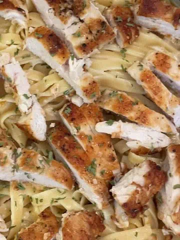 One pan chicken Alfredo with creamy sauce, tender chicken strips, and fettuccine pasta served in a skillet.