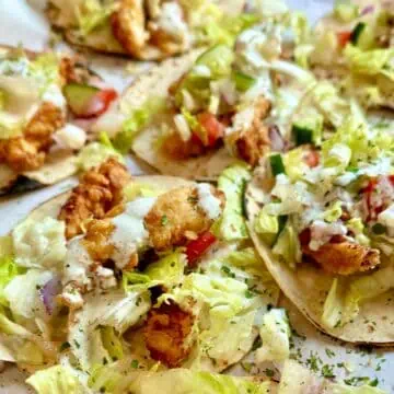 Taco plate featuring buttermilk chicken tenders, homemade ranch, and vibrant toppings like tomatoes, cucumbers, and lettuce.