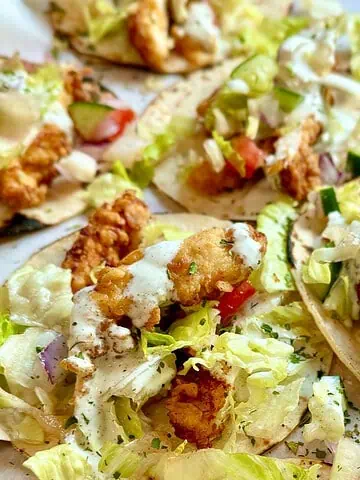 Taco plate featuring buttermilk chicken tenders, homemade ranch, and vibrant toppings like tomatoes, cucumbers, and lettuce.