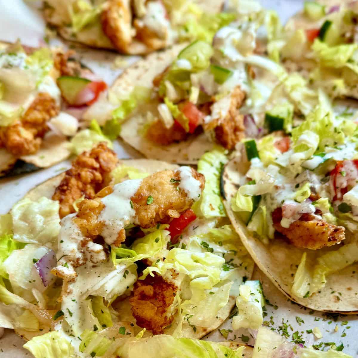 Taco plate featuring buttermilk chicken tenders, homemade ranch, and vibrant toppings like tomatoes, cucumbers, and lettuce.