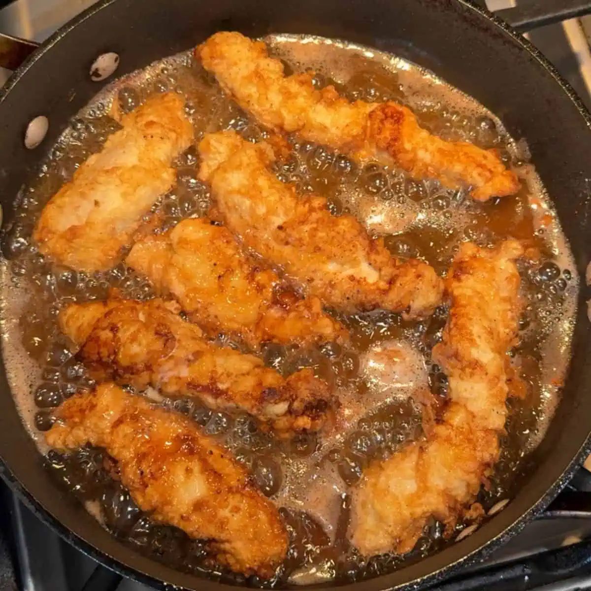 Golden brown chicken tenders frying in a skillet.