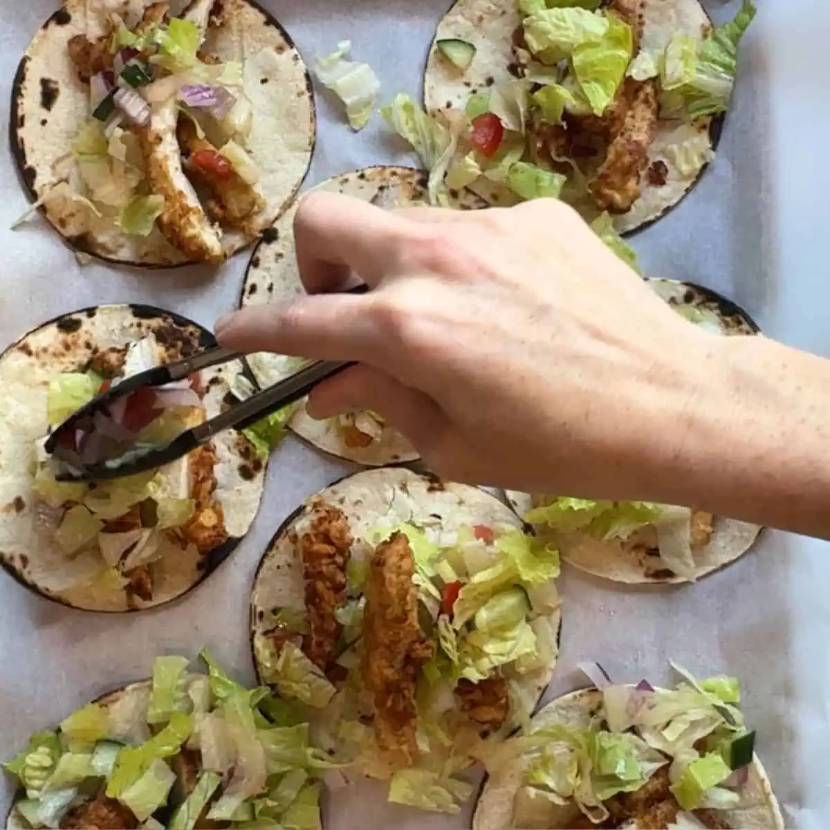 Assembling tacos with crispy chicken tenders, ranch, and fresh toppings.