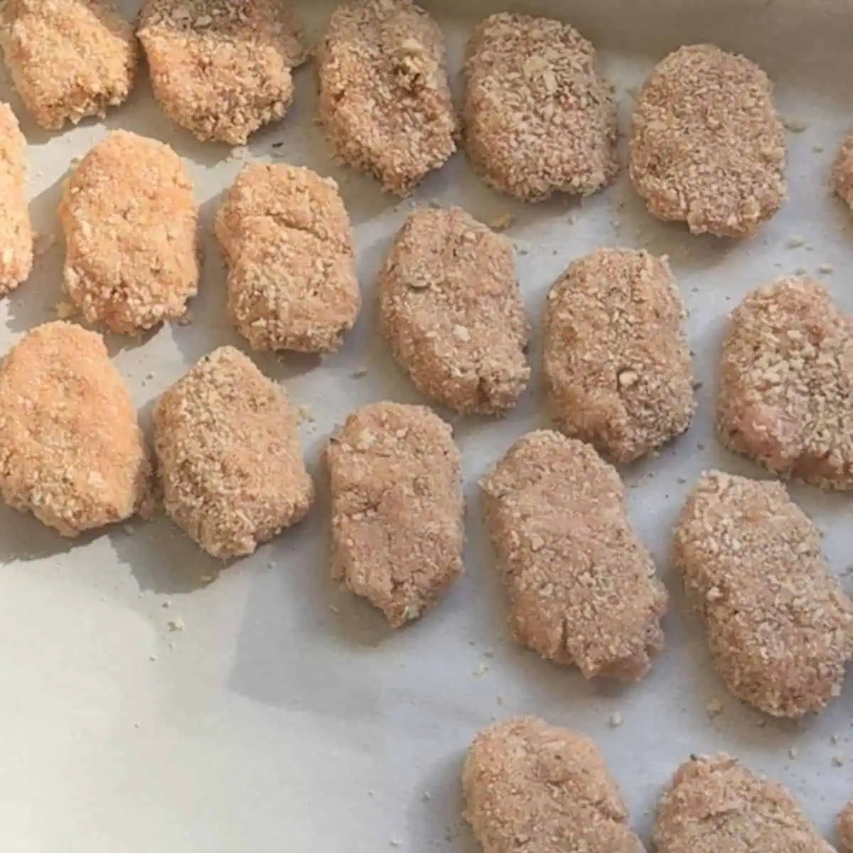 Chicken nuggets lined up on parchment paper ready for baking