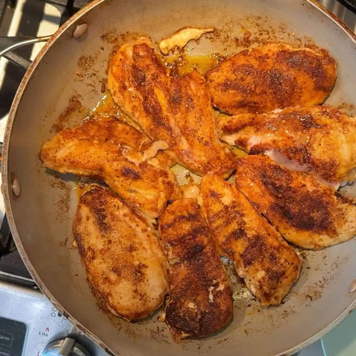 Chicken being sautéed on each side in a pan.