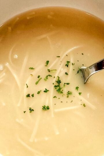 A beautiful bowl of homemade Lemon Egg Drop Soup, garnished with fresh parsley and served with a spoon, showcasing its bright and comforting appearance.