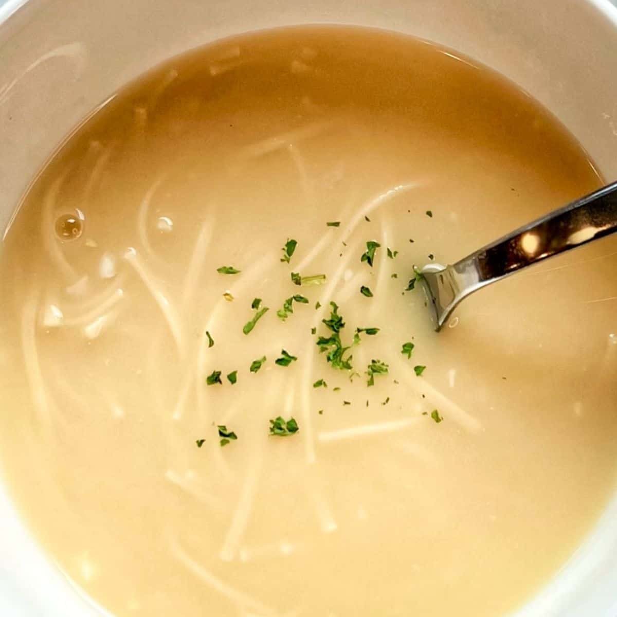 A beautiful bowl of homemade Lemon Egg Drop Soup, garnished with fresh parsley and served with a spoon, showcasing its bright and comforting appearance.