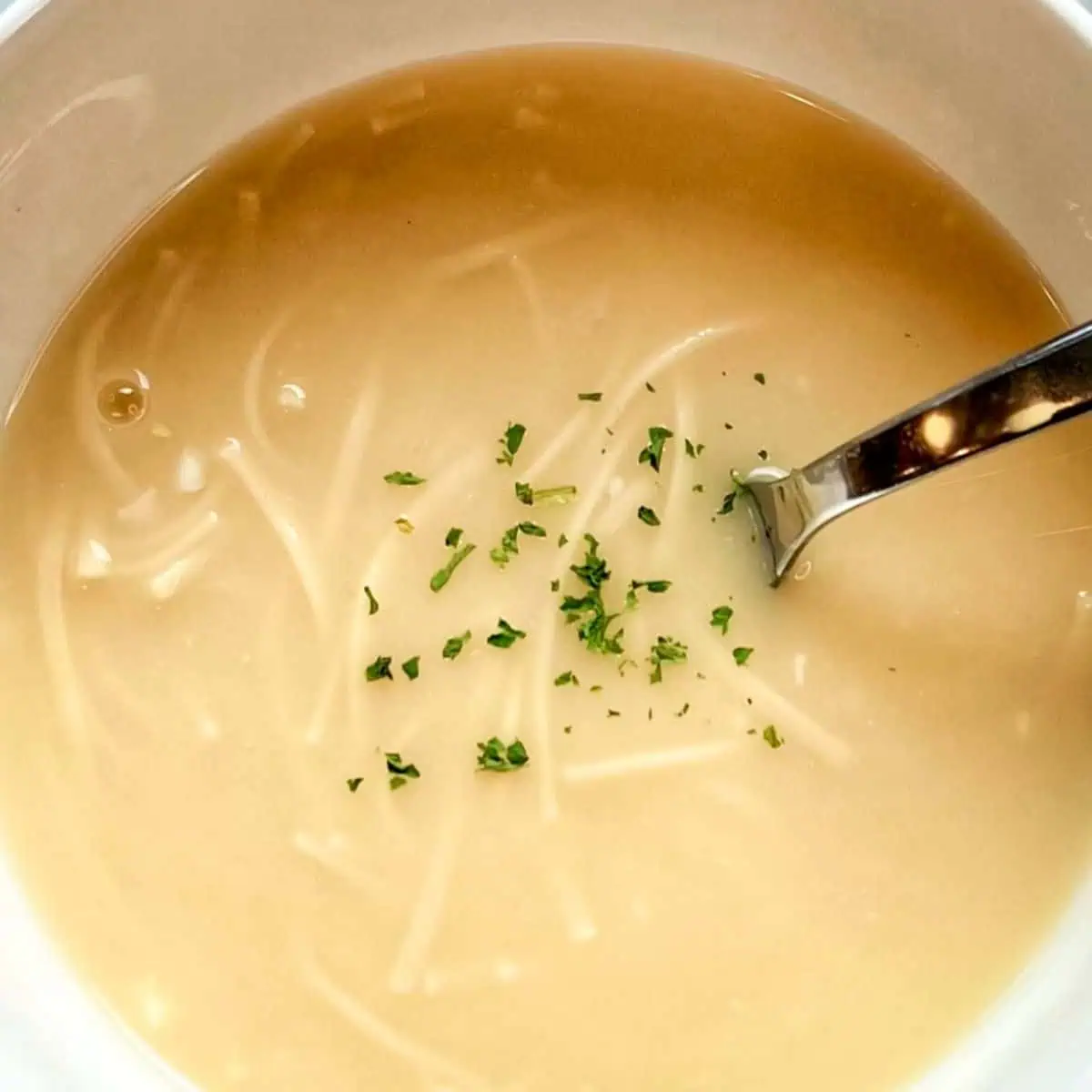 A beautiful bowl of homemade Lemon Egg Drop Soup, garnished with fresh parsley and served with a spoon, showcasing its bright and comforting appearance.