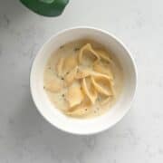 A bowl of creamy Armenian yogurt soup with shell pasta, garnished with dried mint and a drizzle of olive oil