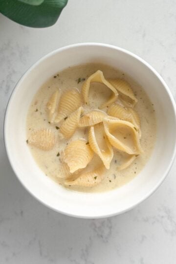 A bowl of creamy Armenian yogurt soup with shell pasta, garnished with dried mint and a drizzle of olive oil