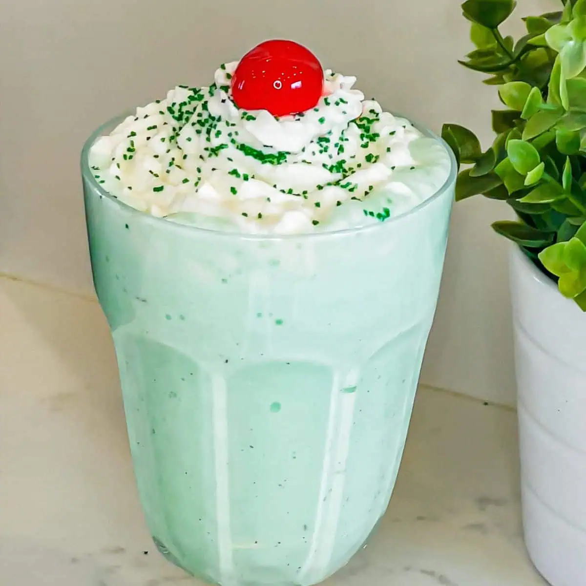 A beautifully styled Shamrock Shake in a tall glass, topped with whipped cream, and a cherry.