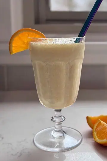 A chilled glass of homemade Orange Julius with a straw and a fresh orange slice.