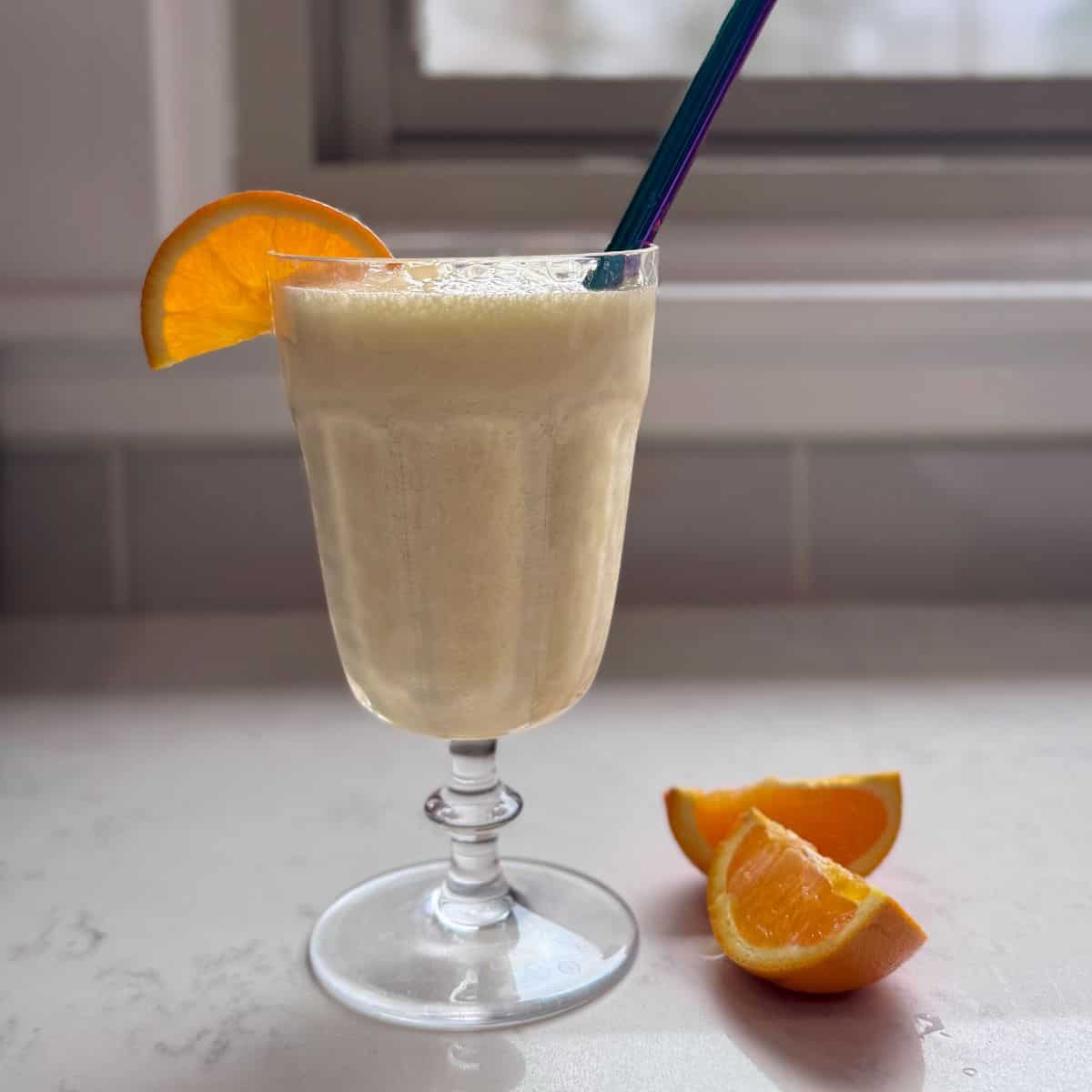 A chilled glass of homemade Orange Julius with a straw and a fresh orange slice.