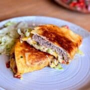 Close-up showing the inside layers of tortilla, beef patty, melted cheese, and pico de gallo.
