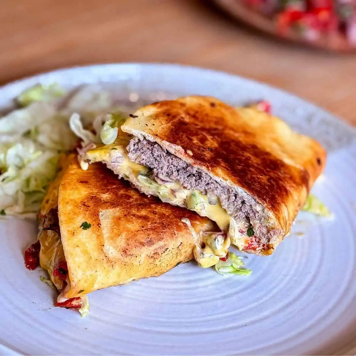 Close-up showing the inside layers of tortilla, beef patty, melted cheese, and pico de gallo.