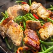 Close-up of chicken thighs, green beans, and sweet peppers cooking in cast iron