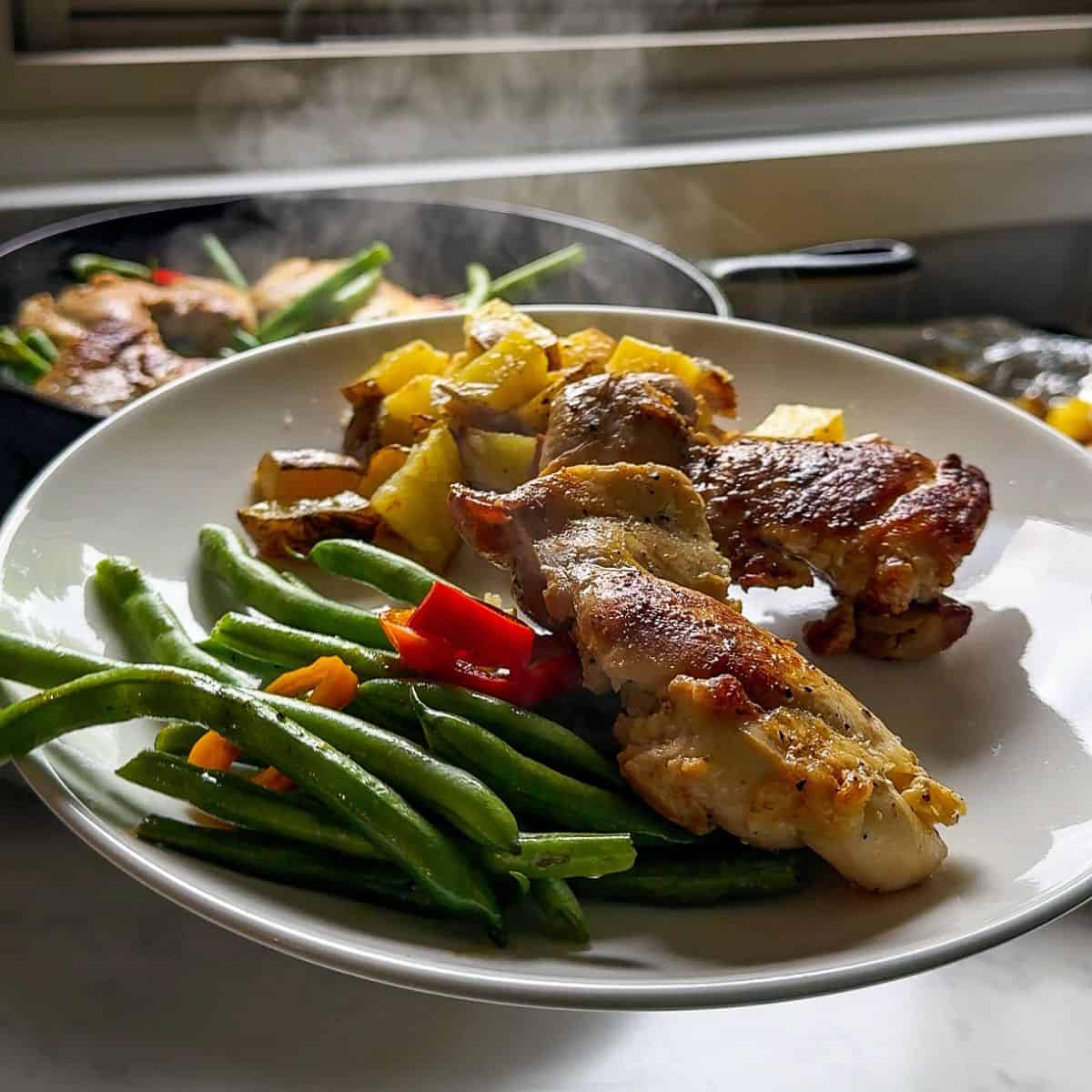 Elevated plate of chicken thighs, green beans, and peppers from cast iron skillet