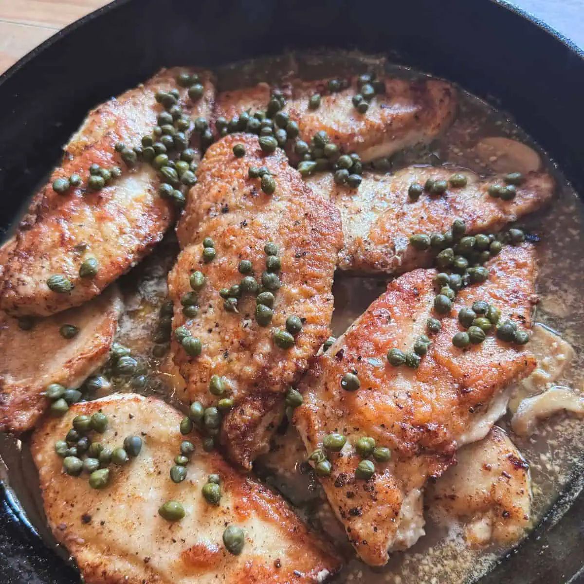 Overhead view of chicken piccata with capers in cast iron on kitchen table