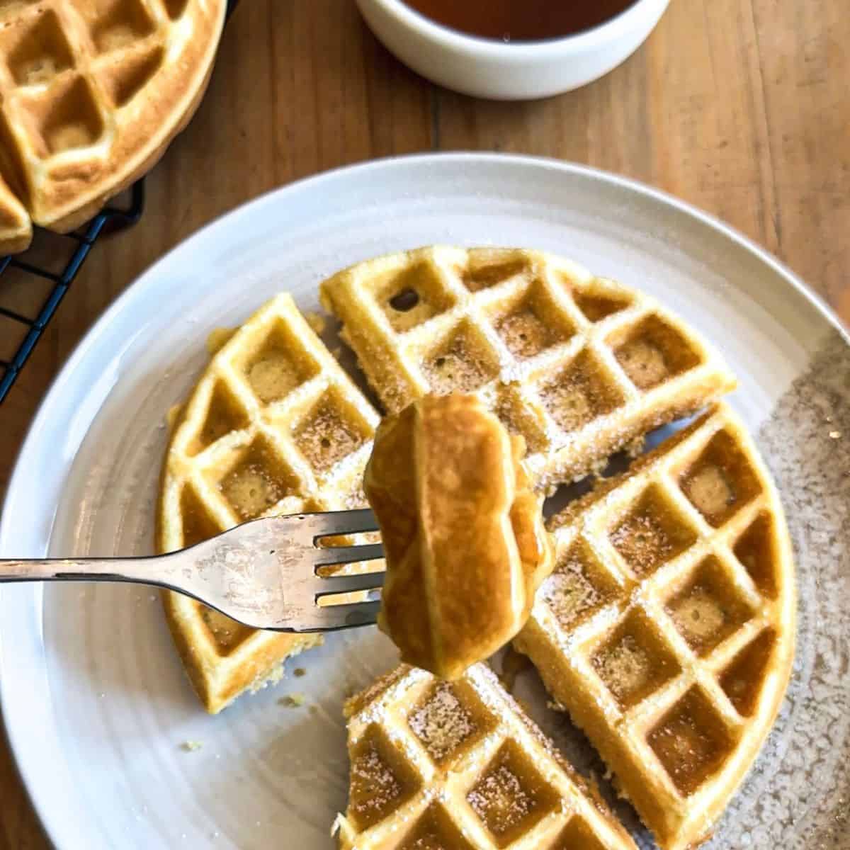 Buttermilk waffle on a fork with full waffles in the background
