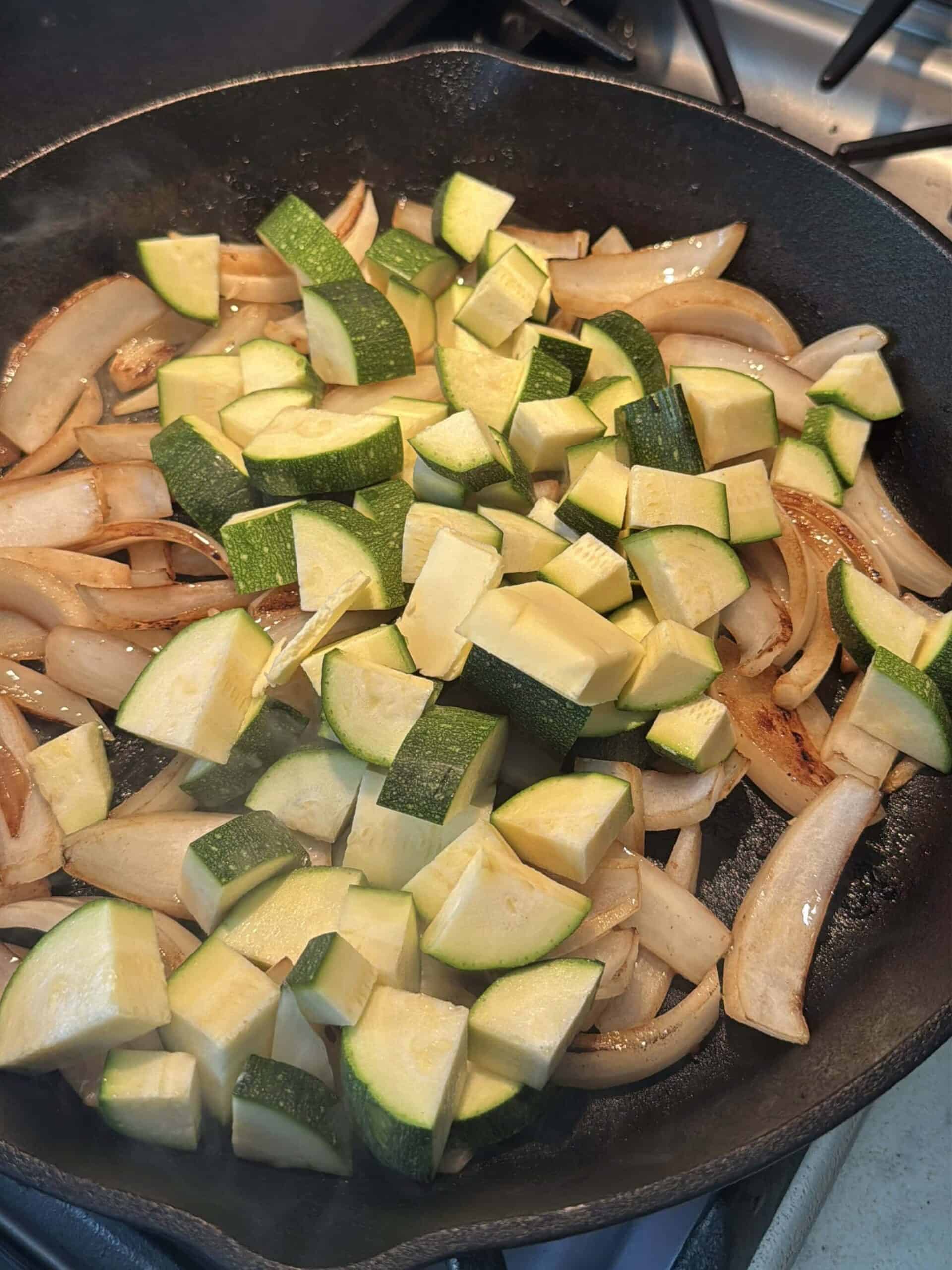 Sliced zucchini and onions sautéing in a hot cast iron skillet.