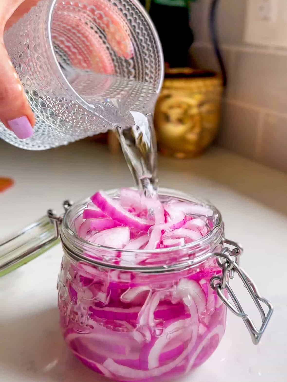 Vinegar and water brine being poured over red onions in a mason jar
