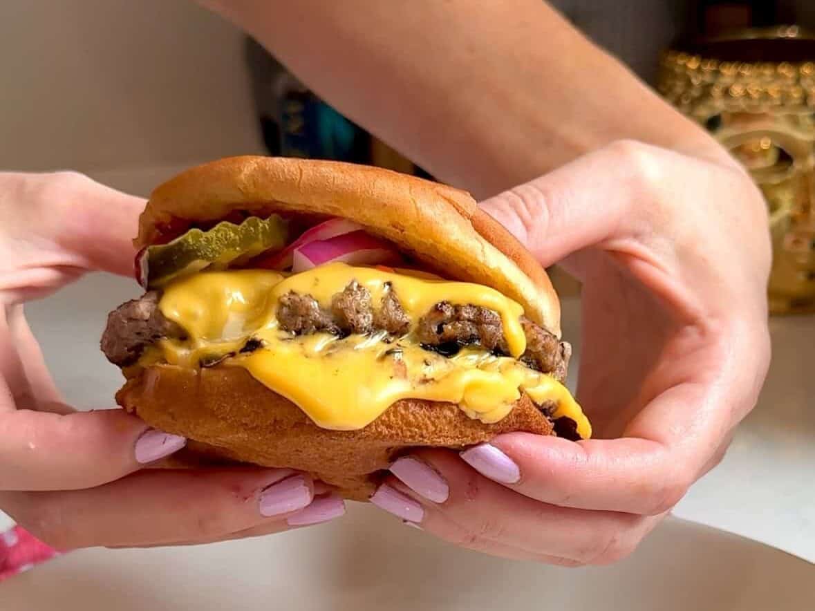 Melted cheese on a smash burger held above a plate