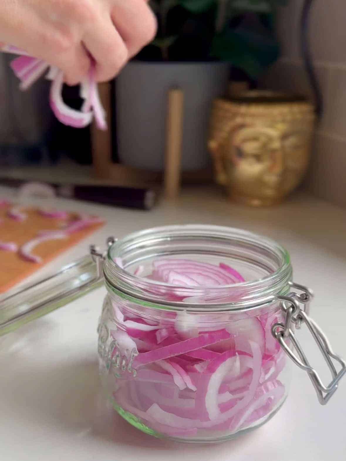 Sliced red onions layered in a clear mason jar before pickling