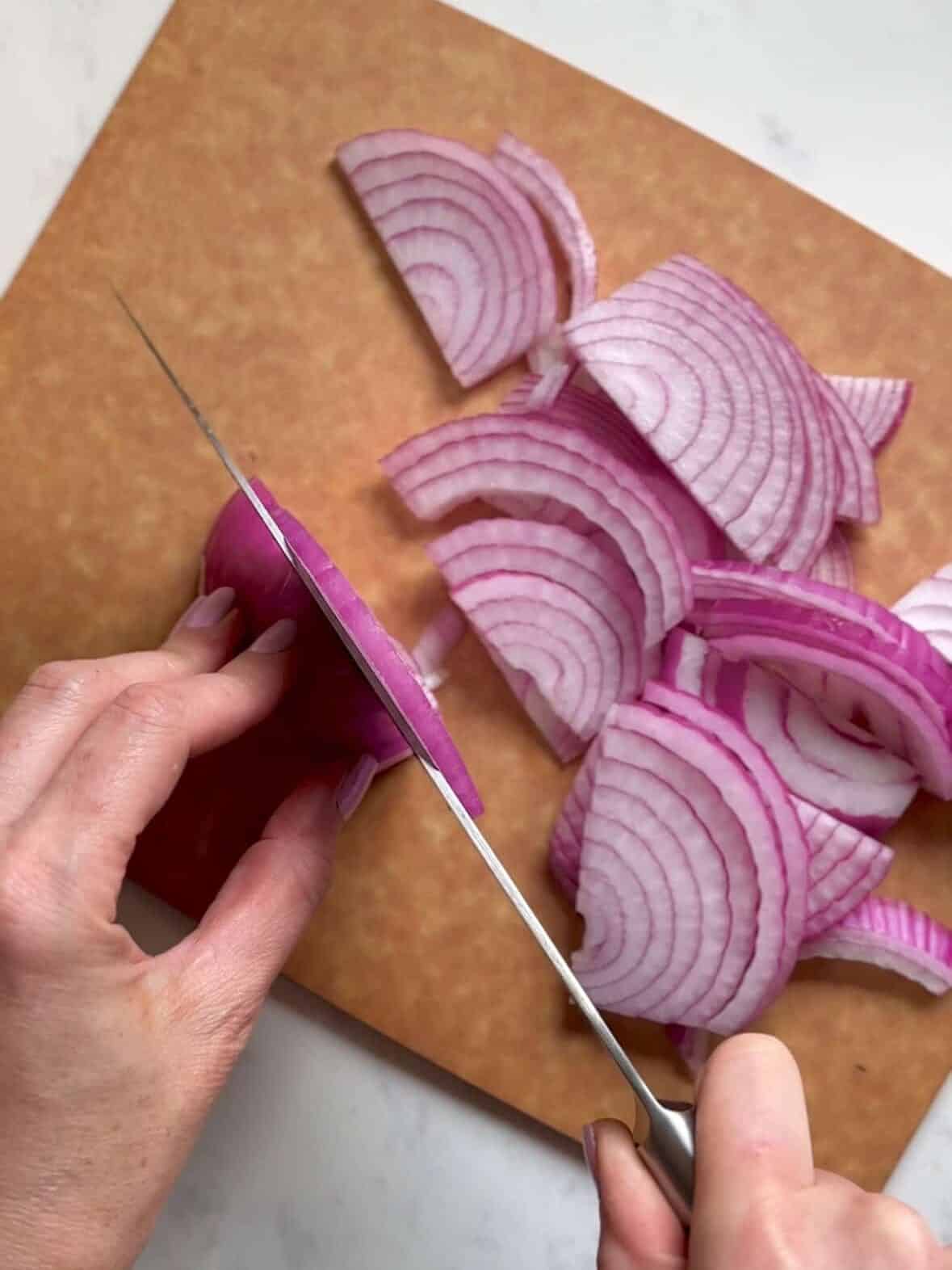 A sharp knife slicing fresh red onions on a wooden cutting board