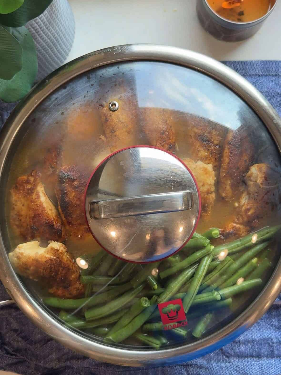 Skillet of chicken, rice, and green beans covered with a lid while cooking