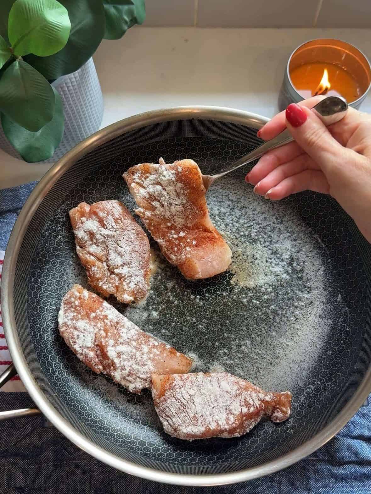 Raw chicken tenders being added to a skillet for one pan chicken and rice