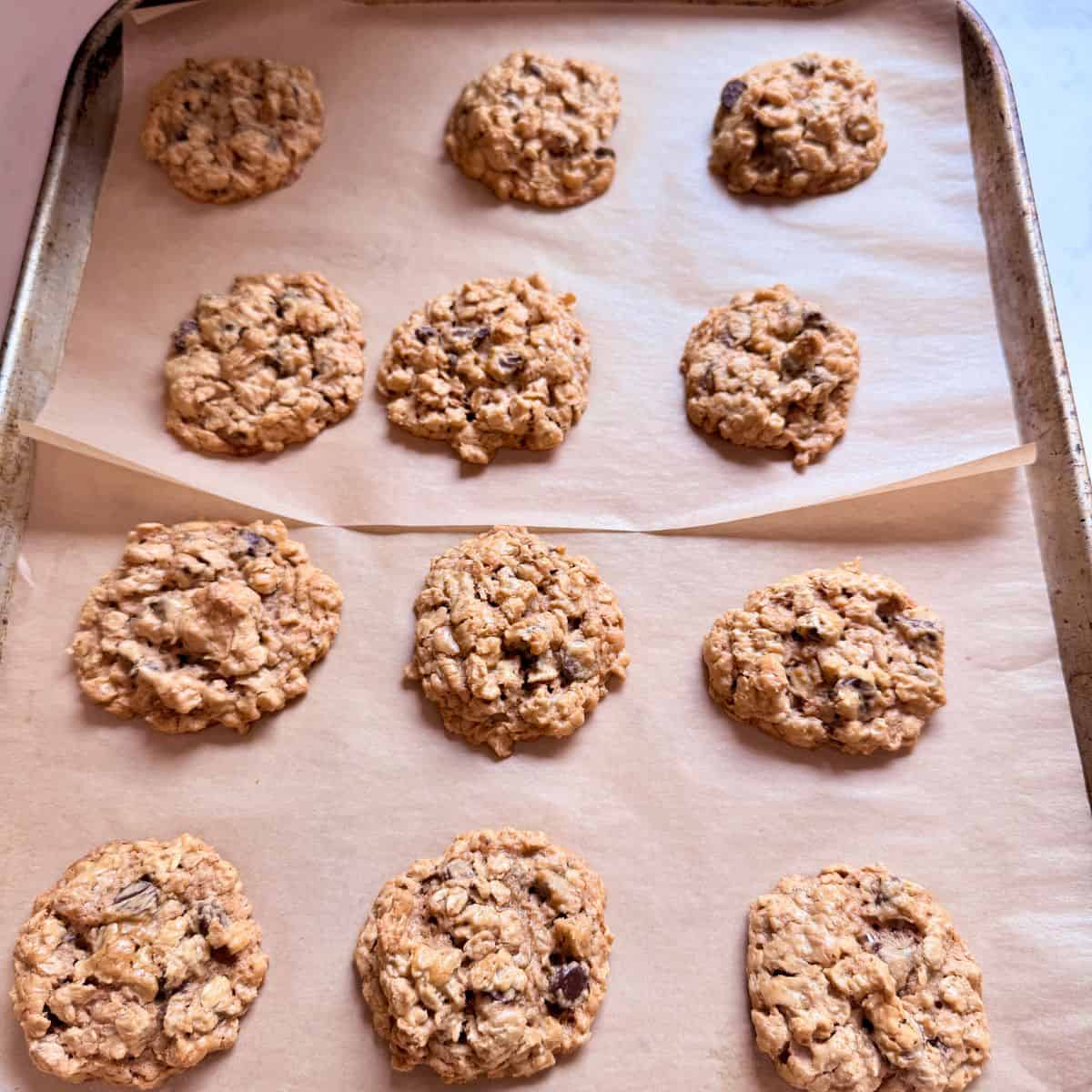 Freshly baked peanut butter oatmeal chocolate chip cookies on a parchment-lined baking tray.
