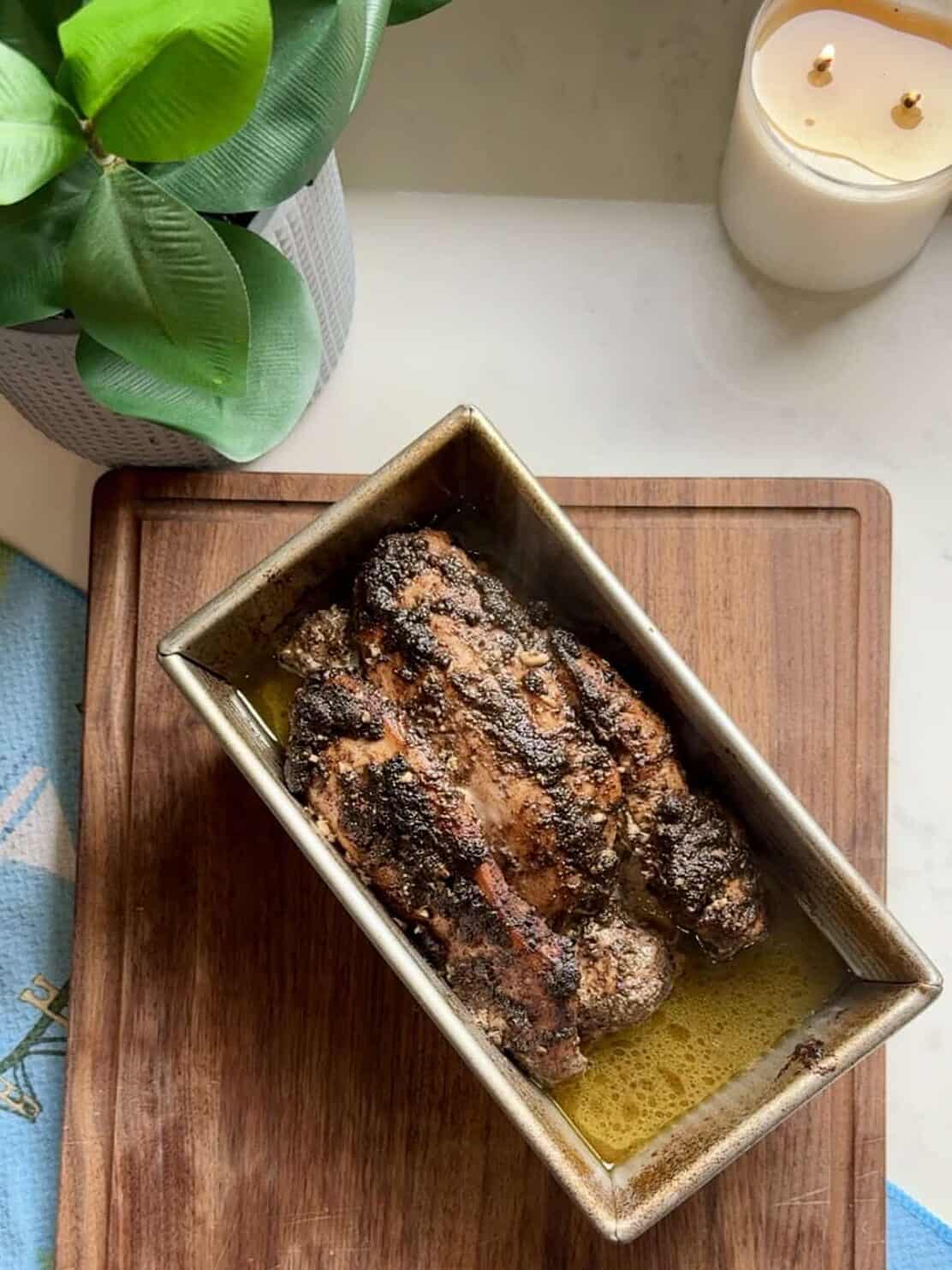 Raw chicken shawarma layered in a loaf pan on a wooden cutting board before cooking.