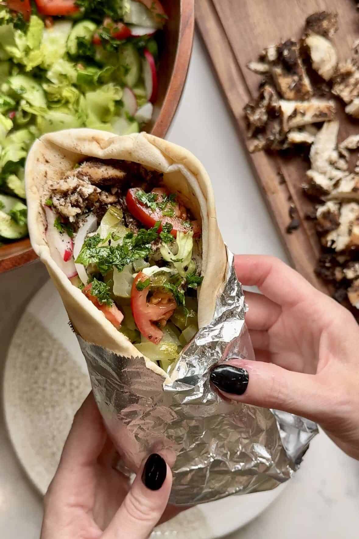 Chicken shawarma wrap filled with lettuce, onions, pickles, hummus, and tomatoes