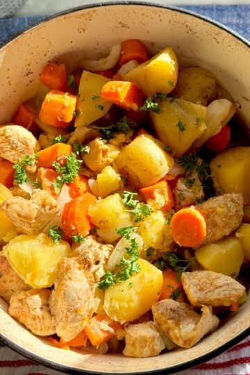 Overhead view of One Pot Chicken and Vegetable Stew in a pot with chunks of chicken, carrots, and yellow potatoes.