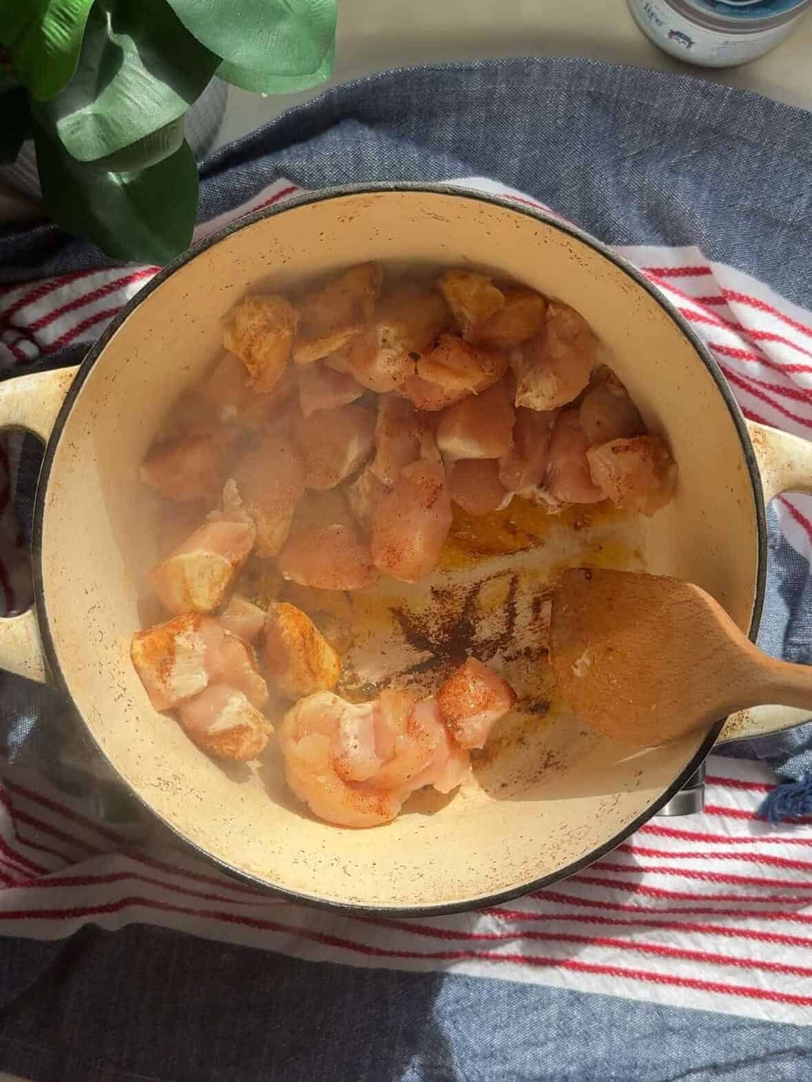 Cubed chicken searing in butter inside a large ceramic pot for One Pot Chicken and Vegetable Stew.
