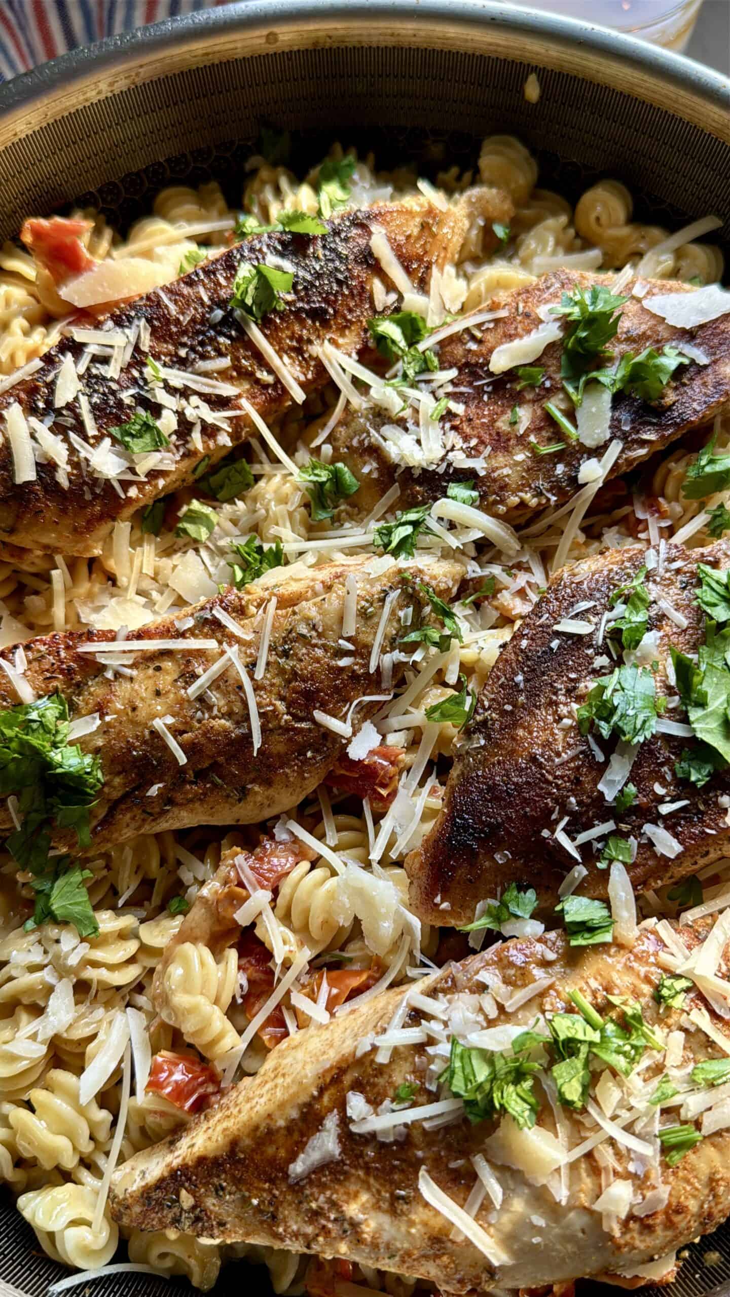 Close-up of creamy sun-dried tomato chicken and pasta topped with grated Parmesan and fresh parsley.