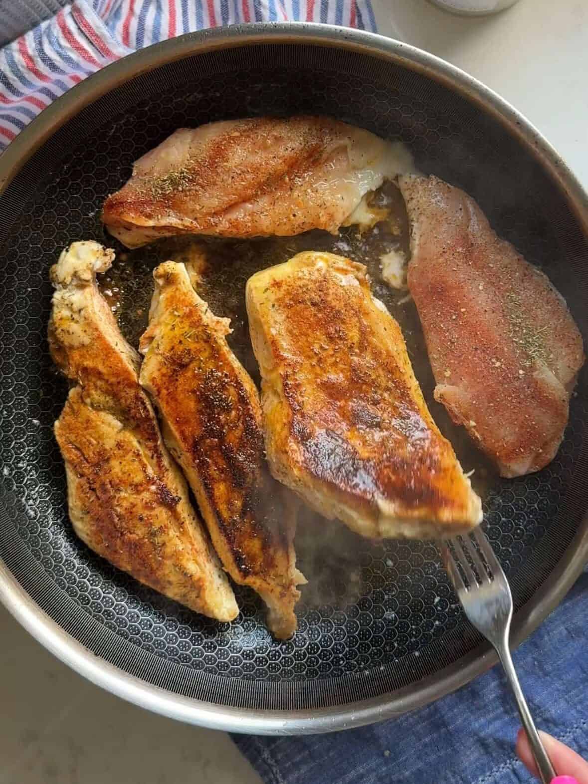 Seasoned chicken strips searing in olive oil in a skillet for creamy sun-dried tomato chicken and pasta.