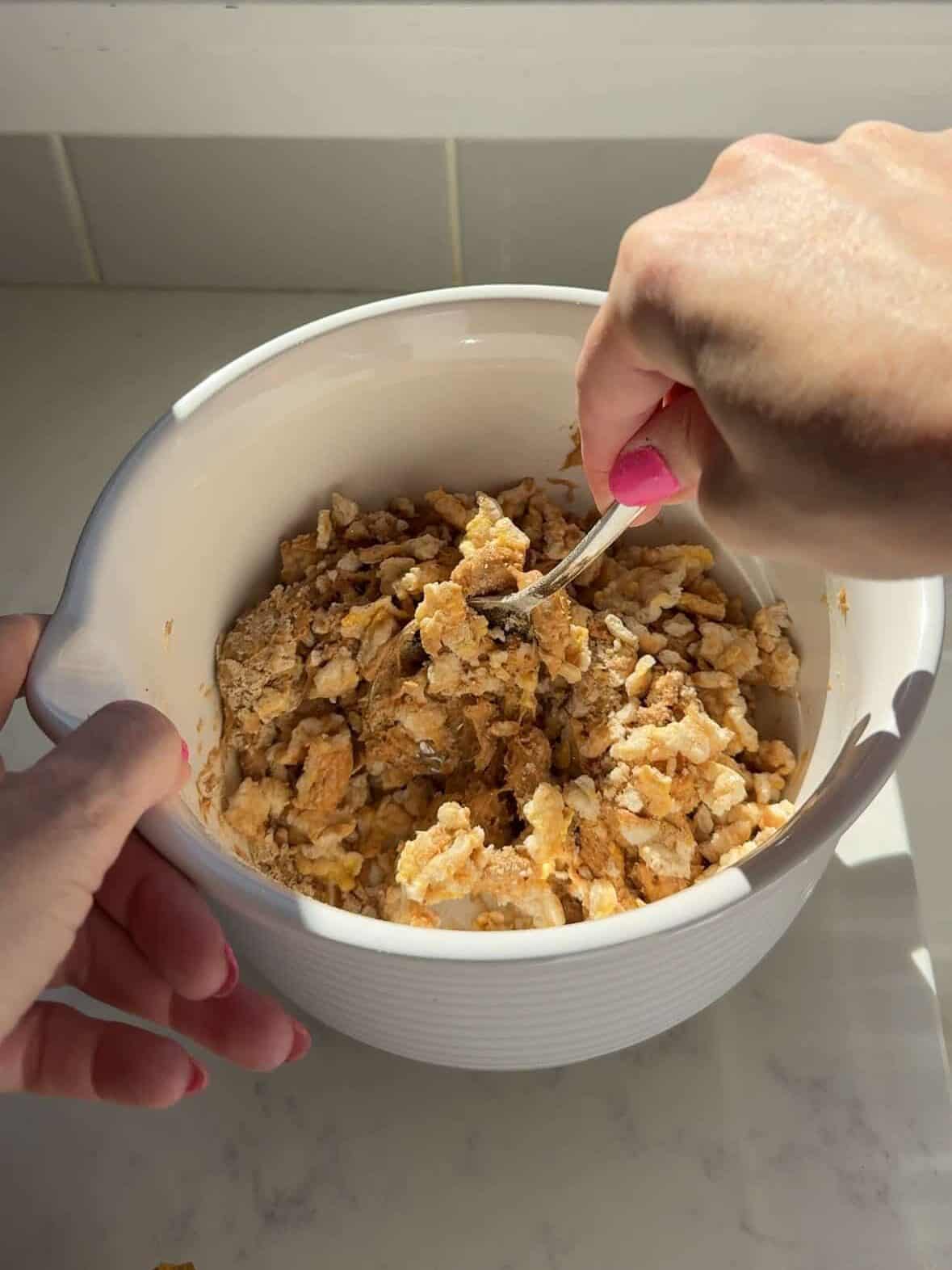 Bowl of peanut butter, protein powder, and crushed rice cakes being mixed together for protein cups.