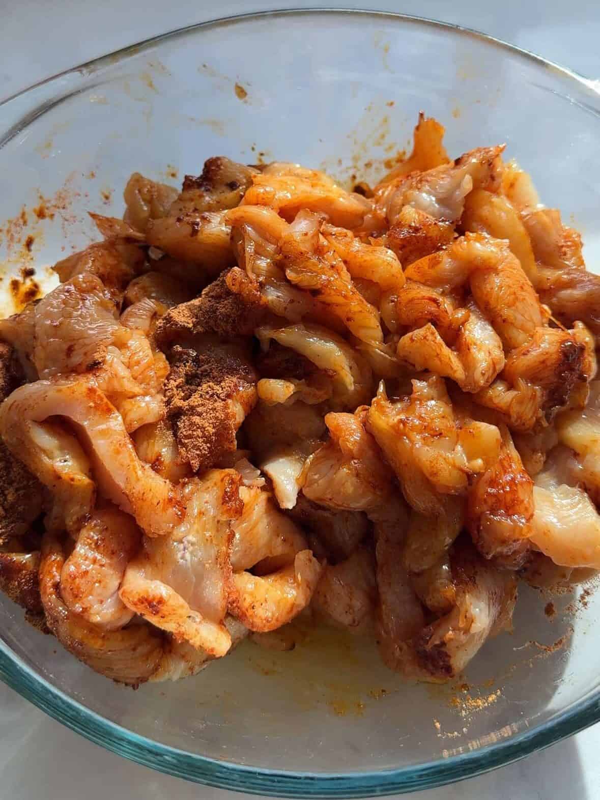 Sliced chicken breasts in a bowl with homemade fajita seasoning, lime juice, and oil ready to marinate.