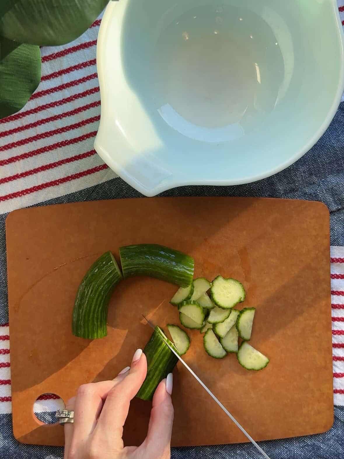 Thinly sliced Persian cucumbers on a cutting board for easy cucumber salad with lemon and sumac.