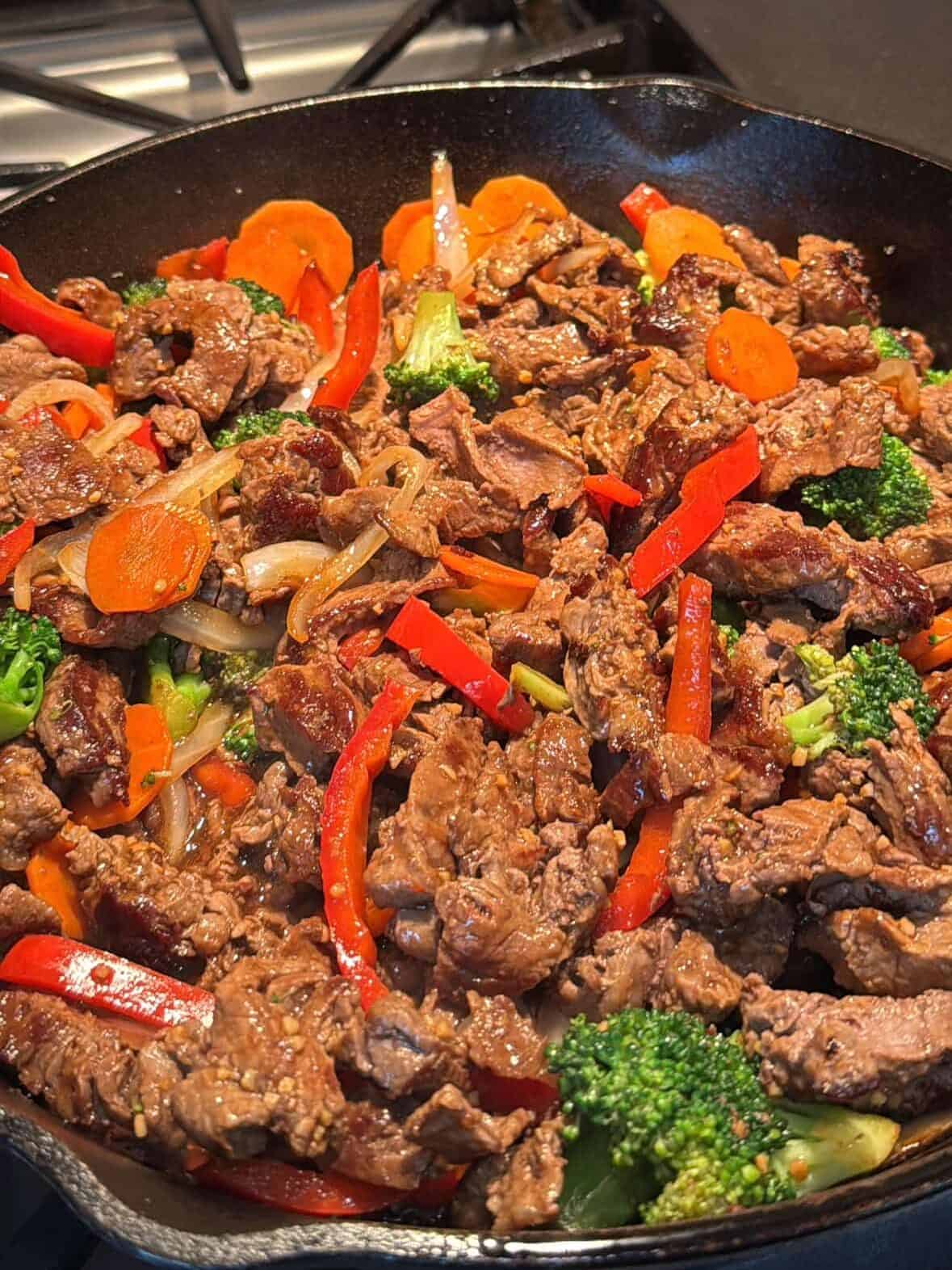 Steak and vegetables tossed together with sauce in cast iron skillet