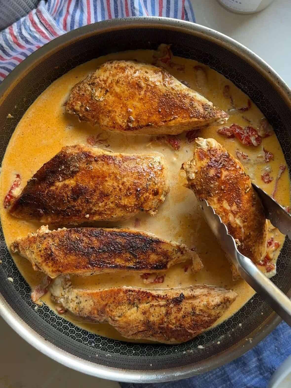 Chicken simmering in creamy sun-dried tomato sauce inside a skillet.