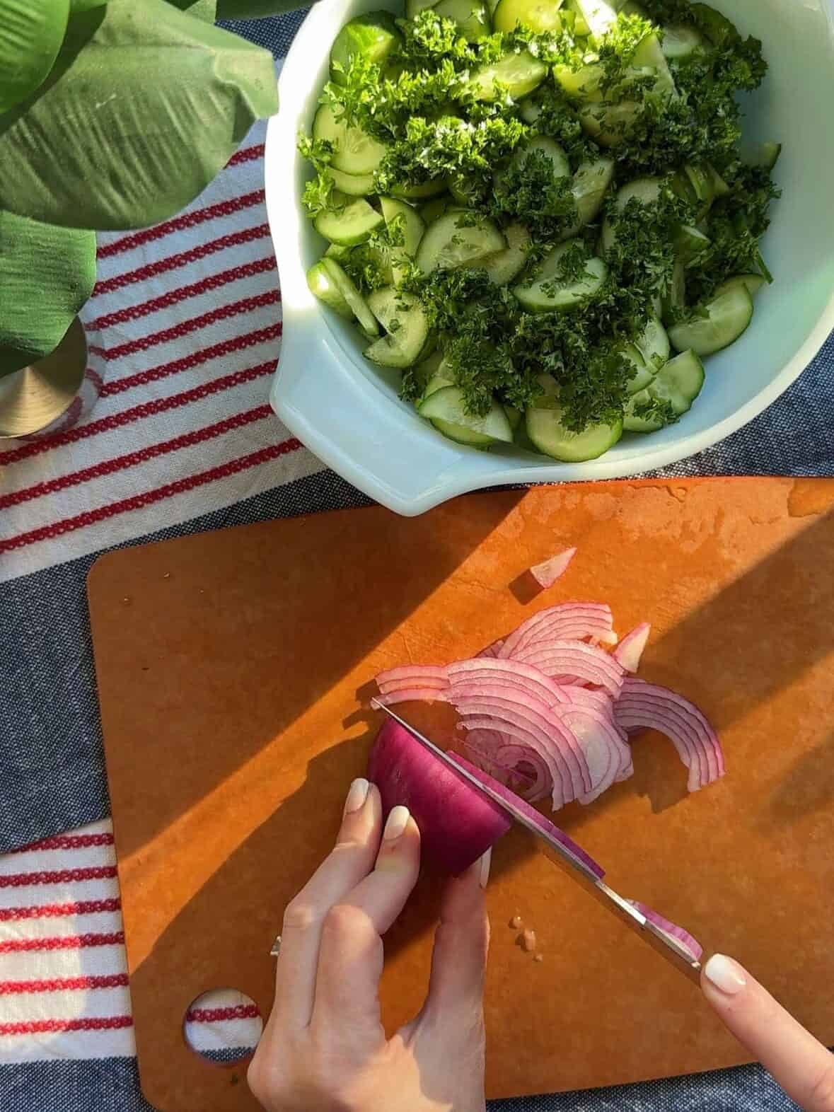 Fresh parsley and thinly sliced red onion on a cutting board for cucumber salad.