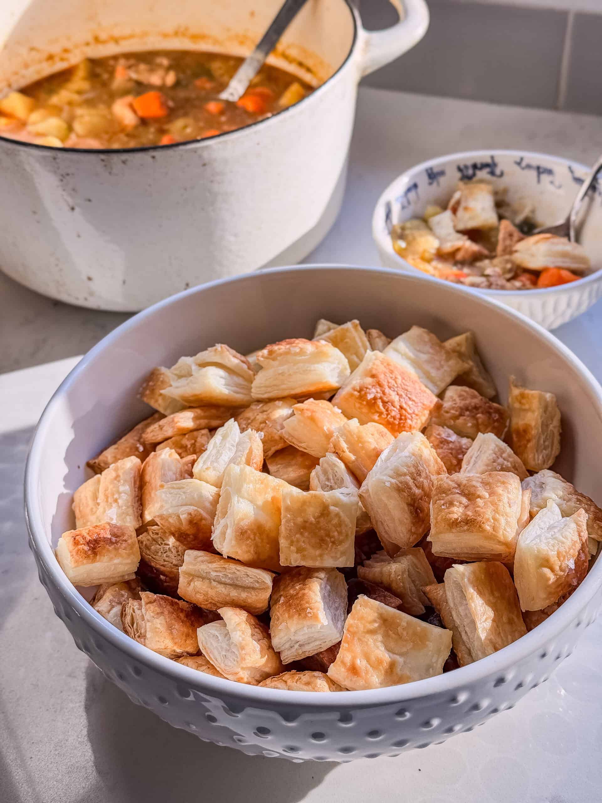Bowl of golden puff pastry croutons next to a pot of chicken vegetable stew