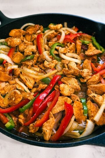 Angled view of sizzling chicken fajitas in a cast iron pan with golden sear marks.