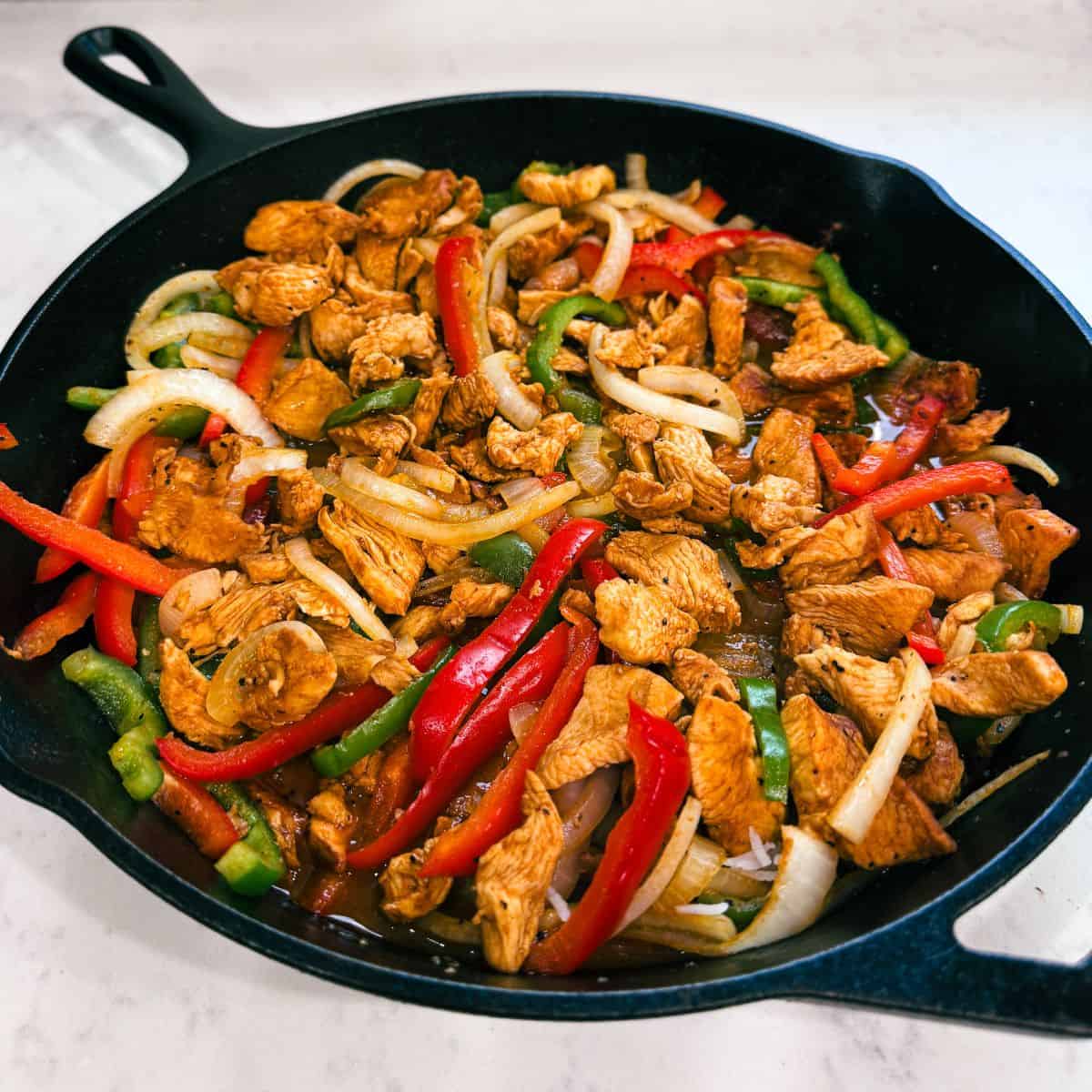 Angled view of sizzling chicken fajitas in a cast iron pan with golden sear marks.