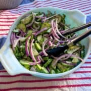 Overhead angled view of cucumber salad with parsley, red onion, and sumac.